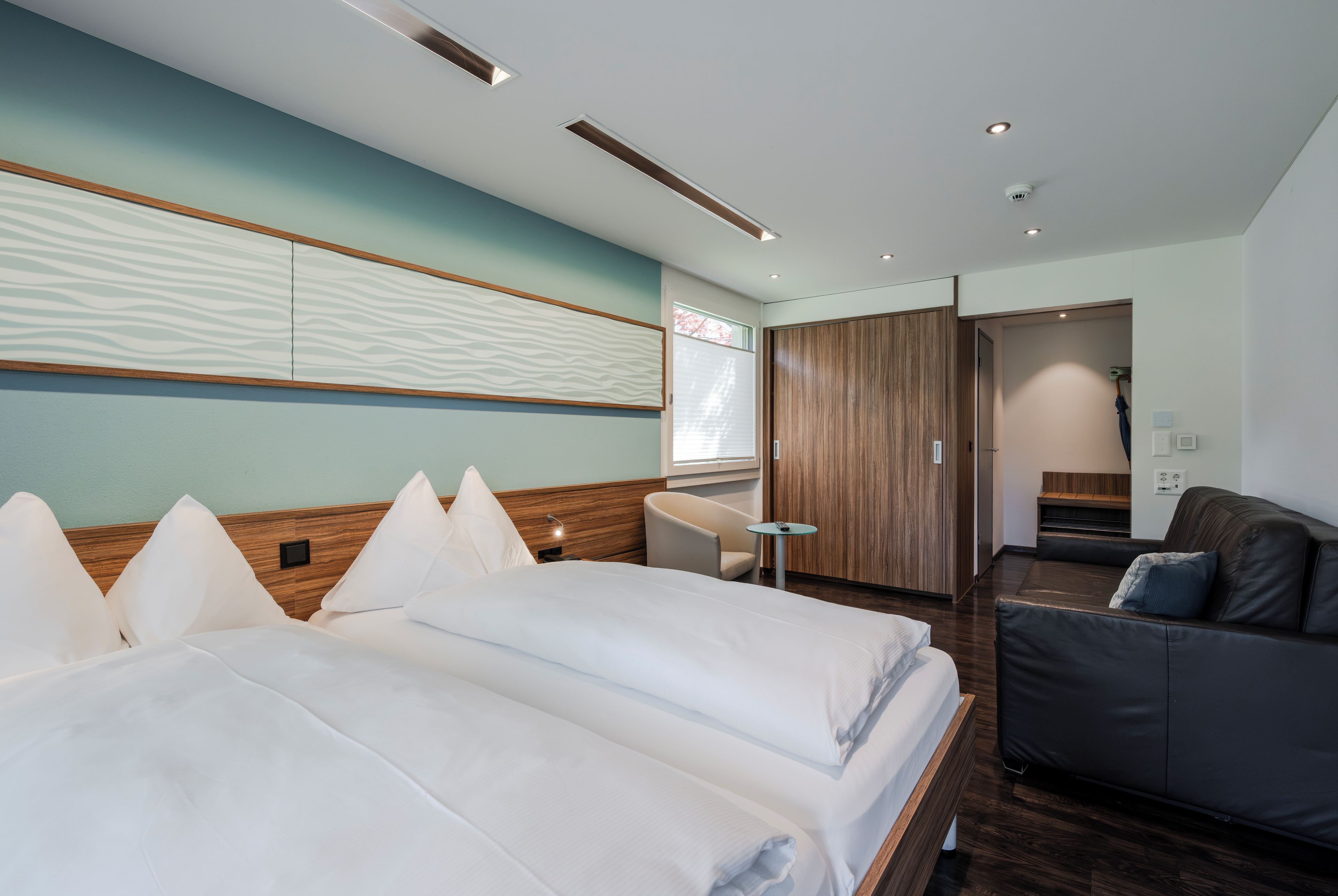 Quarto de hotel moderno com uma cama grande, uma escrivaninha, um sofá e um guarda-roupa.