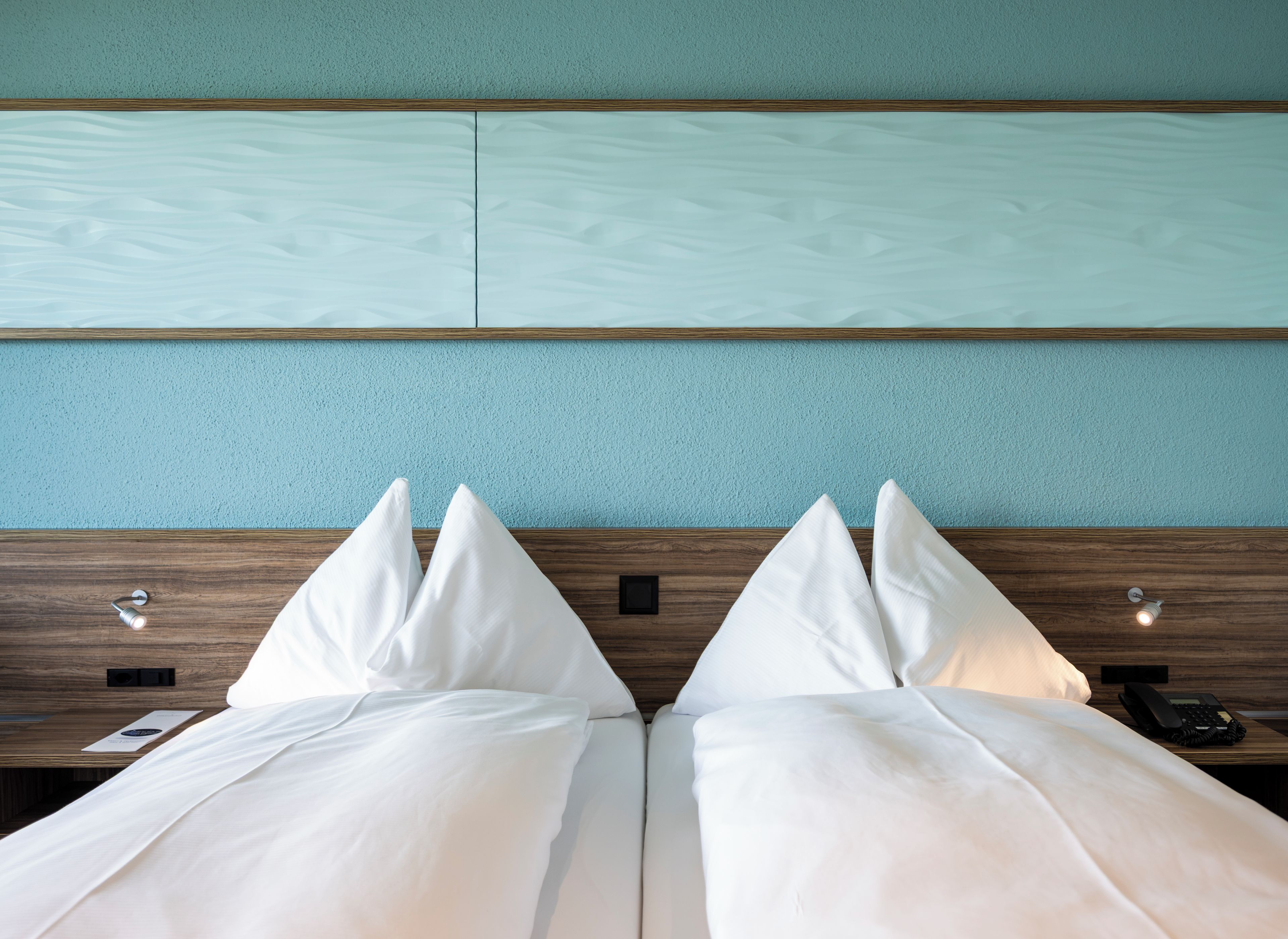 Une chambre d’hôtel avec un lit, des oreillers, une tête de lit en bois et un téléphone fixé au mur.