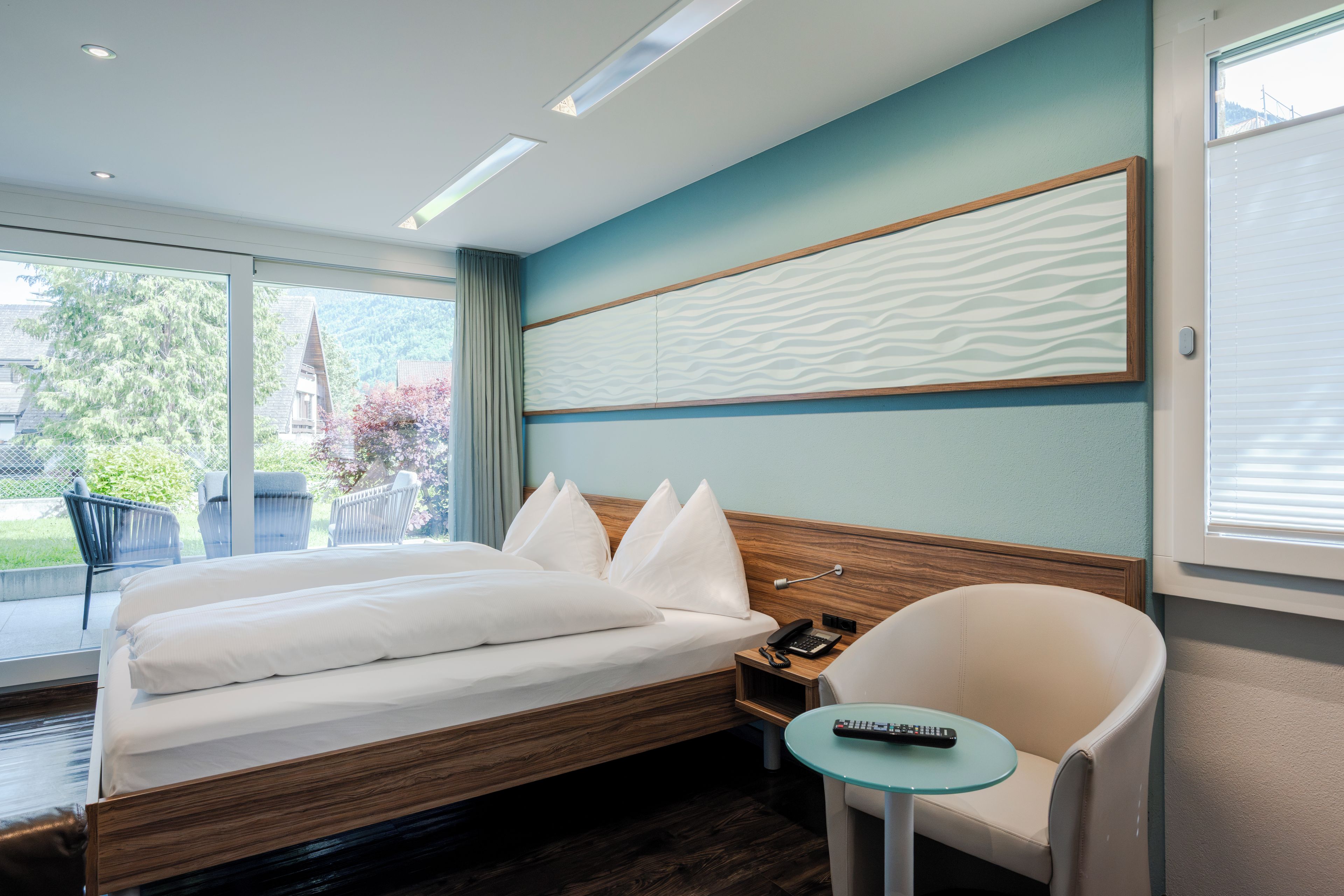 Habitación de hotel moderna con una cama grande, una mesita, una silla y vistas al exterior.