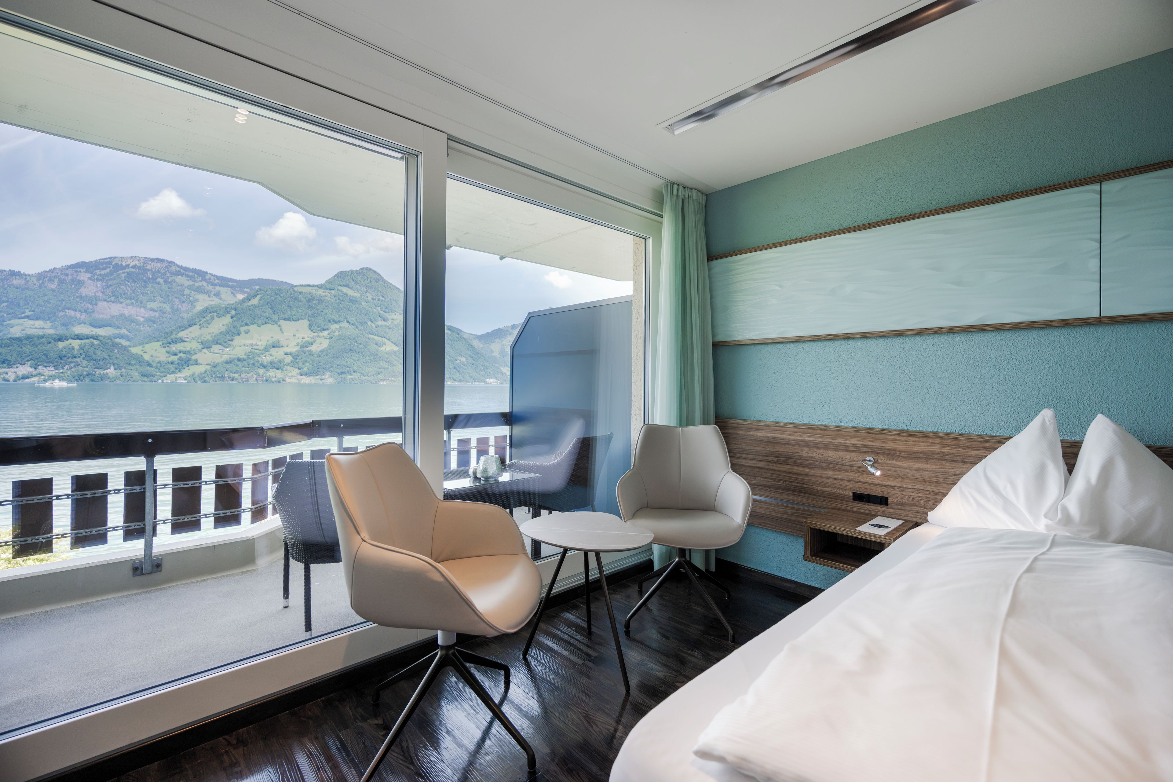 Habitación de hotel con un ventanal grande, una cama, una silla, una mesita y una mesita de noche.