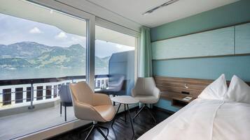 Habitación de hotel con un ventanal grande, una cama, una silla, una mesita y una mesita de noche.