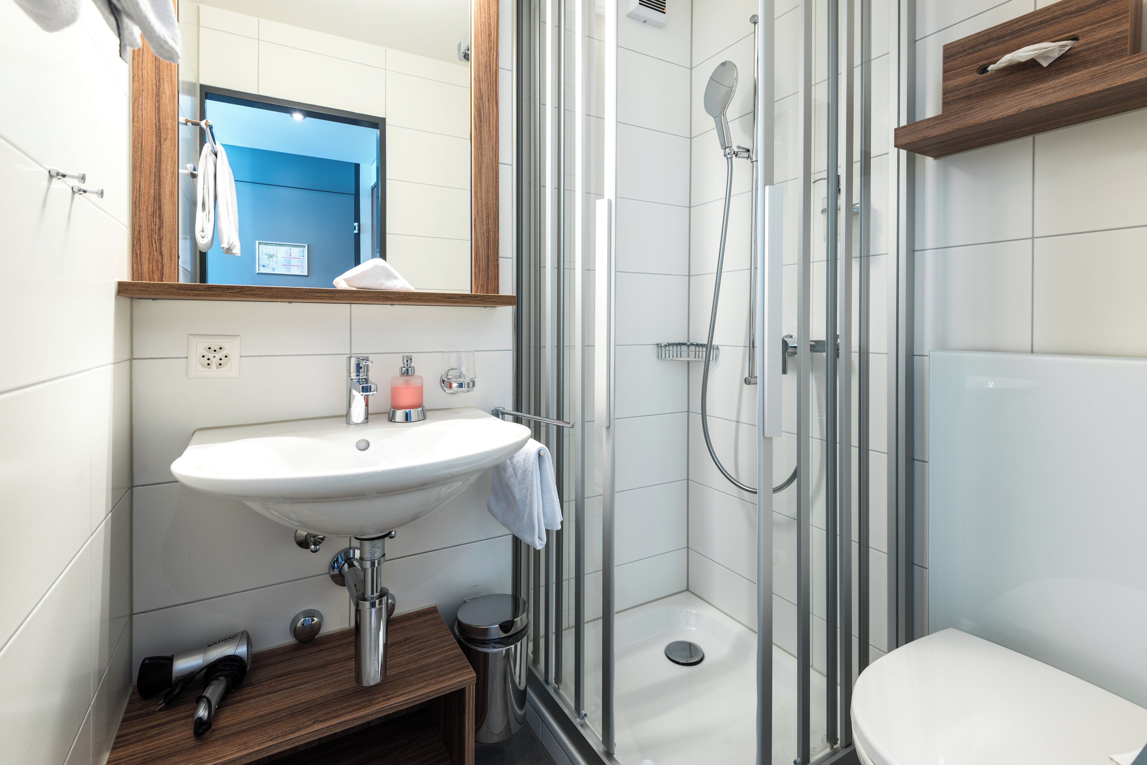 A modern bathroom with a white sink, a mirror, a shower, and a toilet.