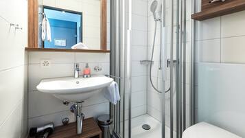 A modern bathroom with a white sink, a mirror, a shower, and a toilet.