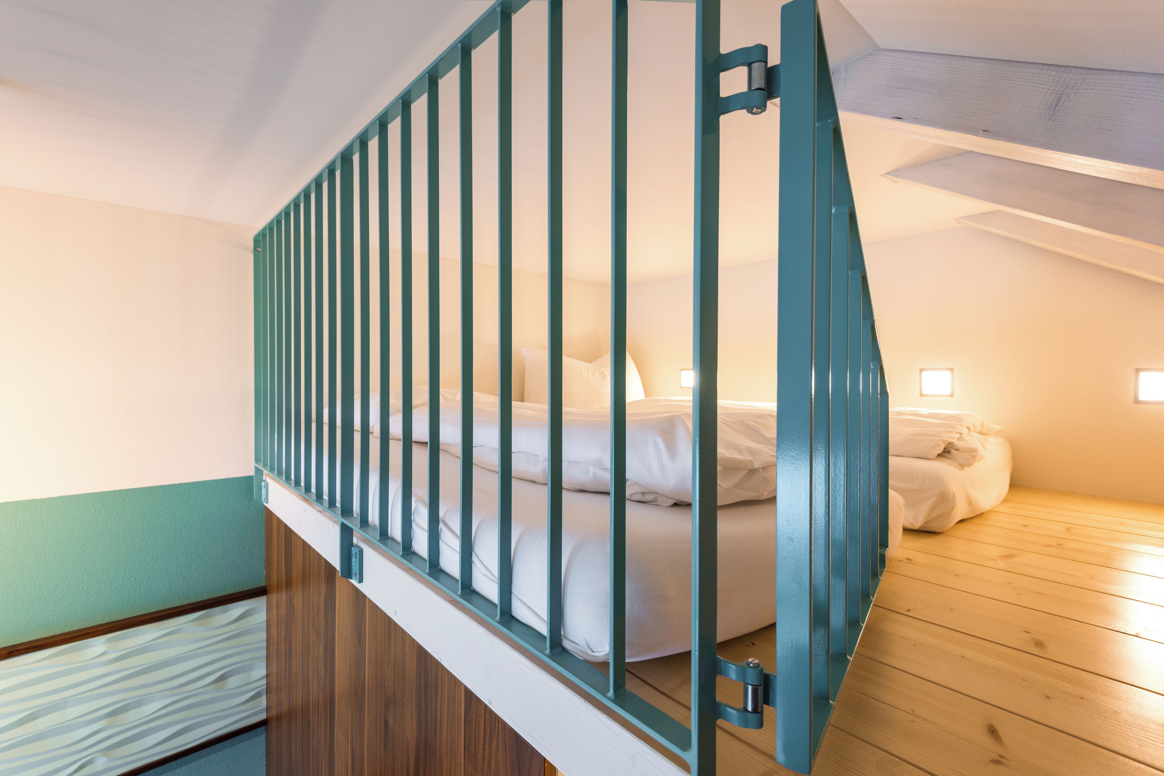 Ein Schlafzimmer mit Holzboden, einem Bett mit weißer Bettwäsche und einem türkisblauen Geländer.