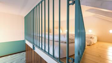 Ein Schlafzimmer mit Holzboden, einem Bett mit weißer Bettwäsche und einem türkisblauen Geländer.