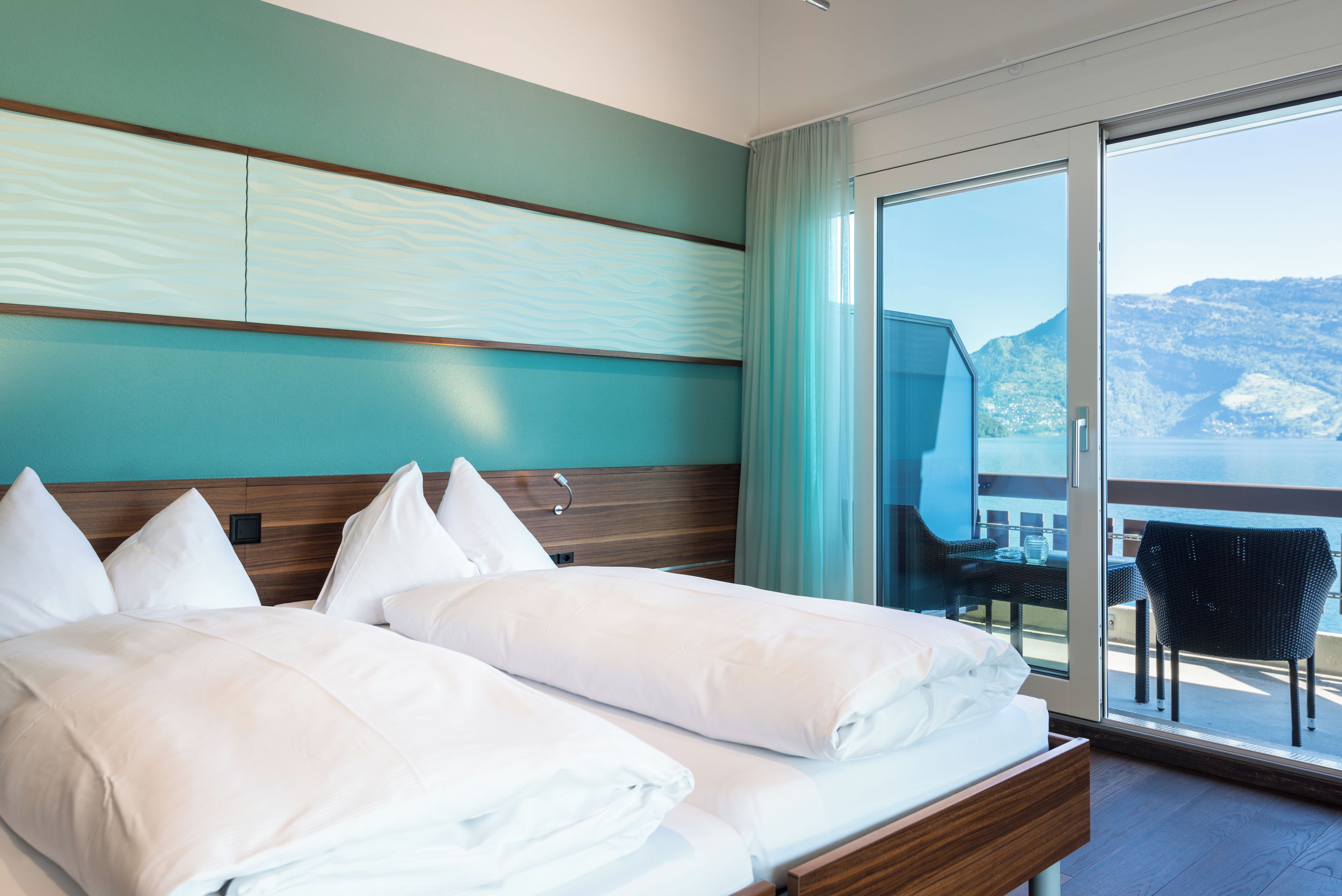 A hotel room with a bed, a view of the sea, and a balcony with a chair.