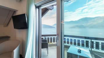 A room with a television, a chair, and a view of a lake and mountains through a large window.