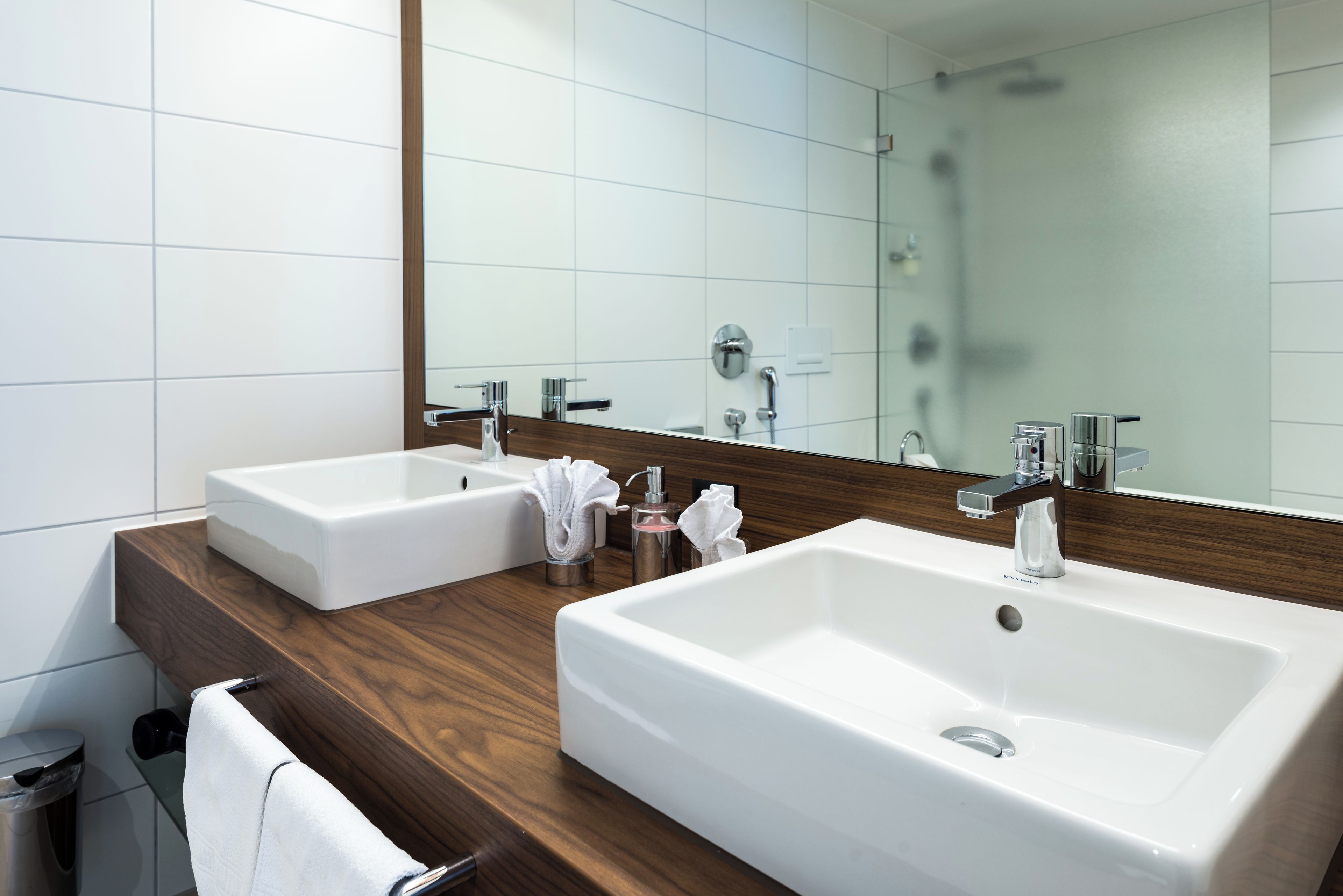 A modern bathroom with two sinks, a large mirror, and a wooden vanity.