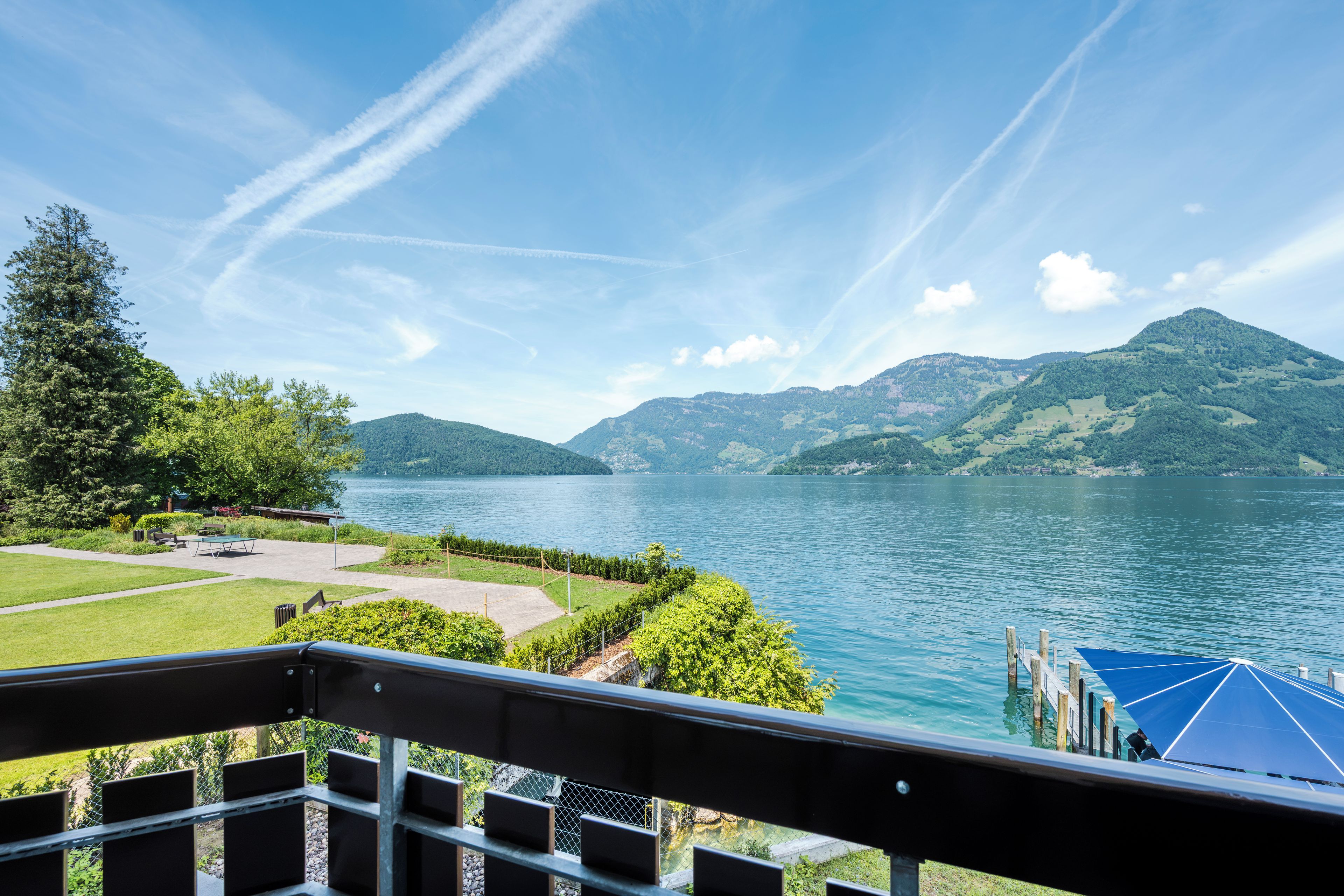 Une vue sur le lac, avec une terrasse surplombant l’eau, le tout entouré de verdure et de montagnes.