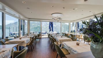Ein Restaurant mit Tischen und Stühlen, große Fenster mit Blick auf die Berge und eine Decke mit Einbaustrahlern.
