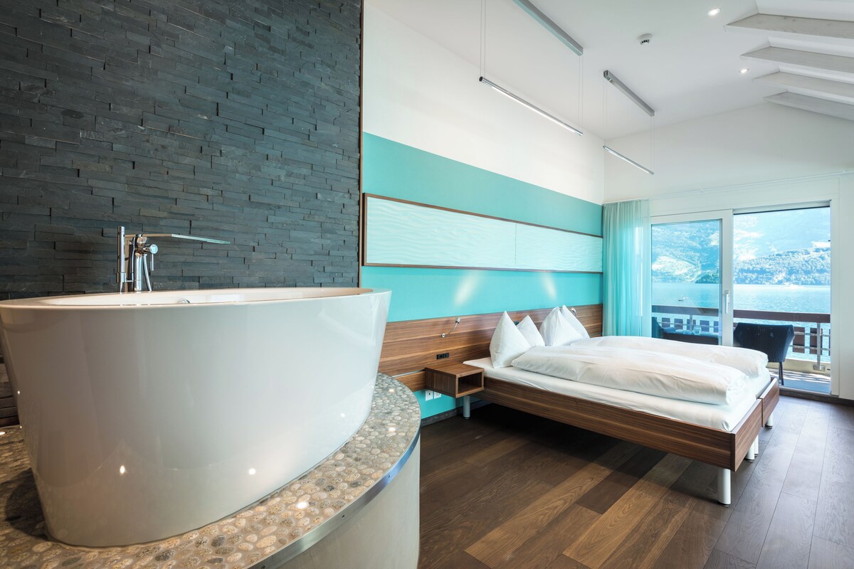 A modern hotel room with a large bathtub, a bed, and a view of the sea.