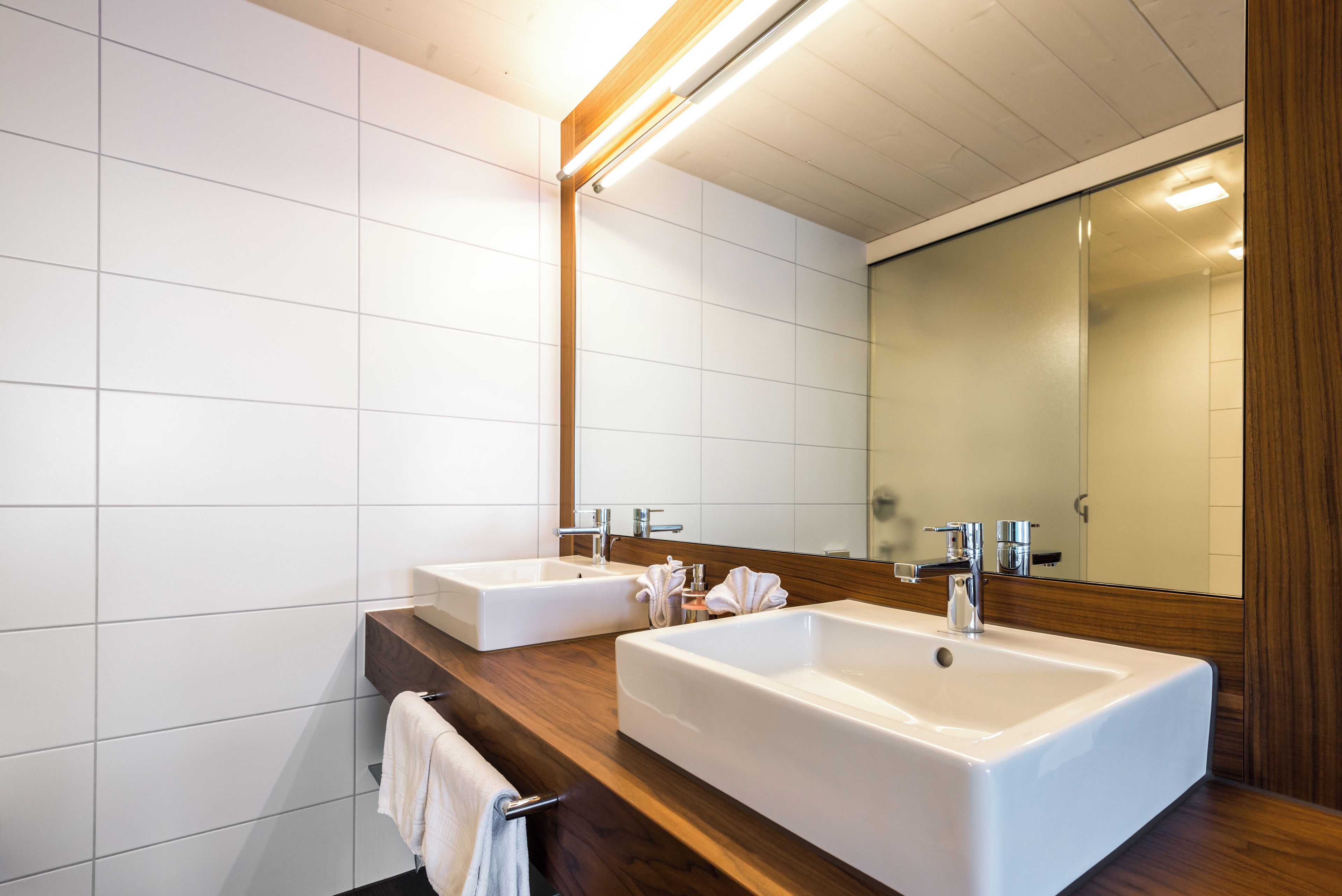 Un baño moderno con dos lavamanos, un mueble de tocador de madera y un espejo grande.