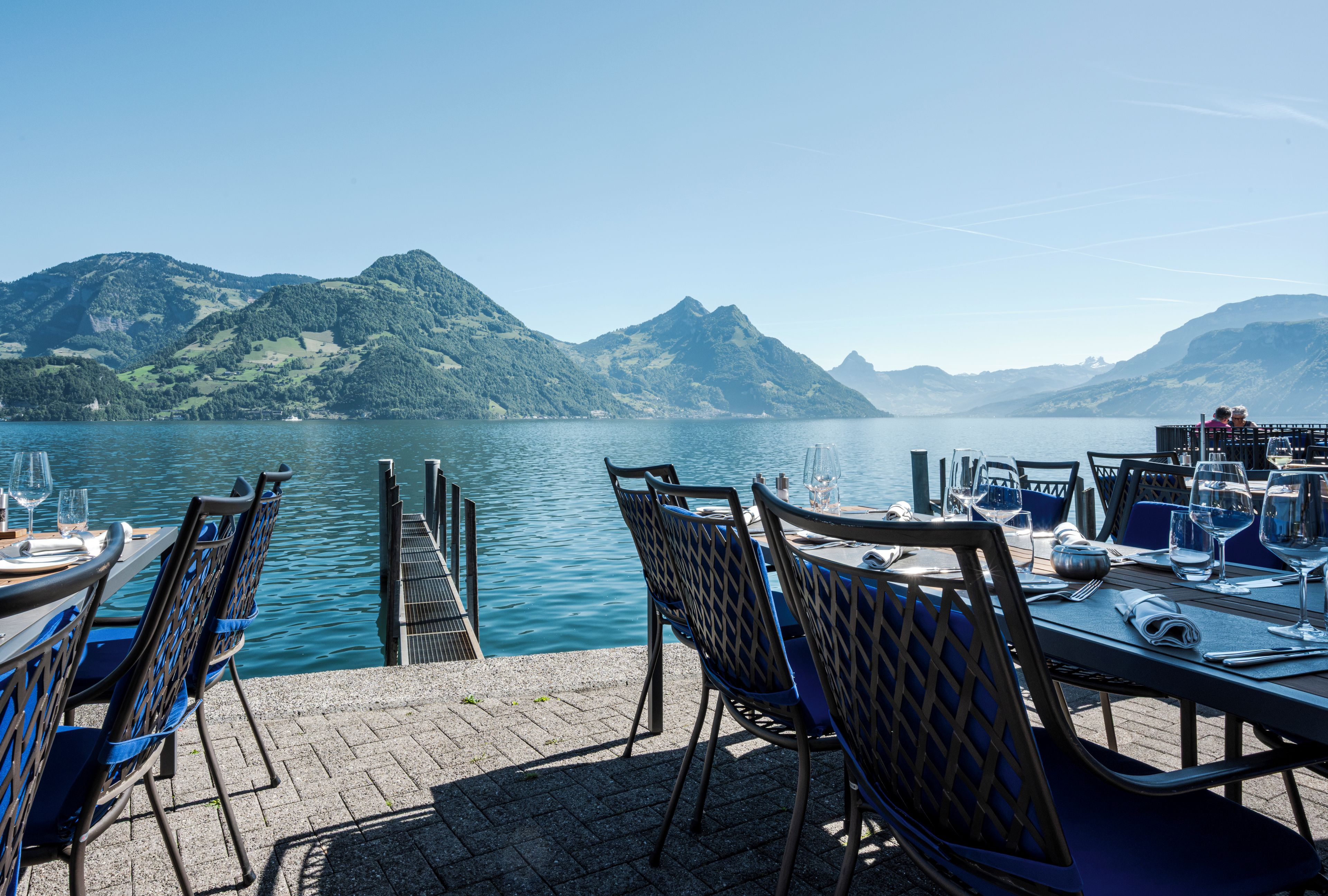 A lakeside restaurant with outdoor seating overlooking a calm lake and mountains.