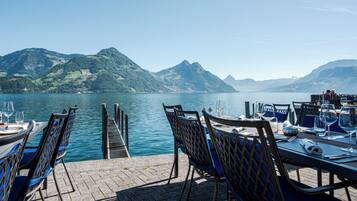 A lakeside restaurant with outdoor seating overlooking a calm lake and mountains.
