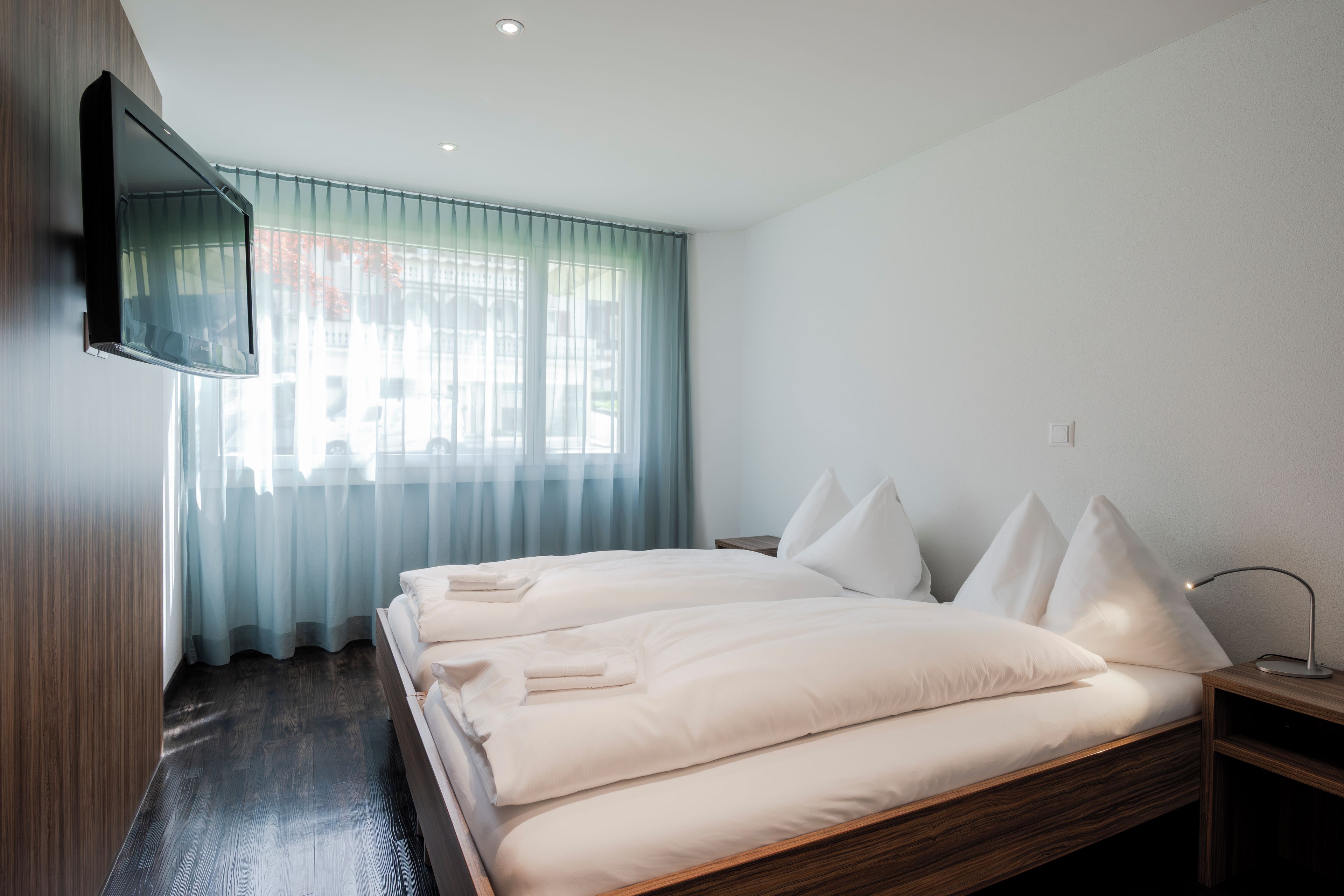 A hotel room with a bed, a TV mounted on the wall, and a window with curtains.