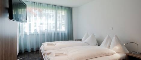 A hotel room with a bed, a TV mounted on the wall, and a window with curtains.