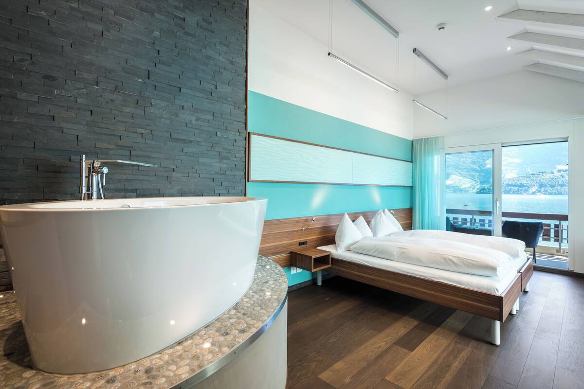 Una habitación de hotel moderna con una bañera grande, una cama y vistas al mar.