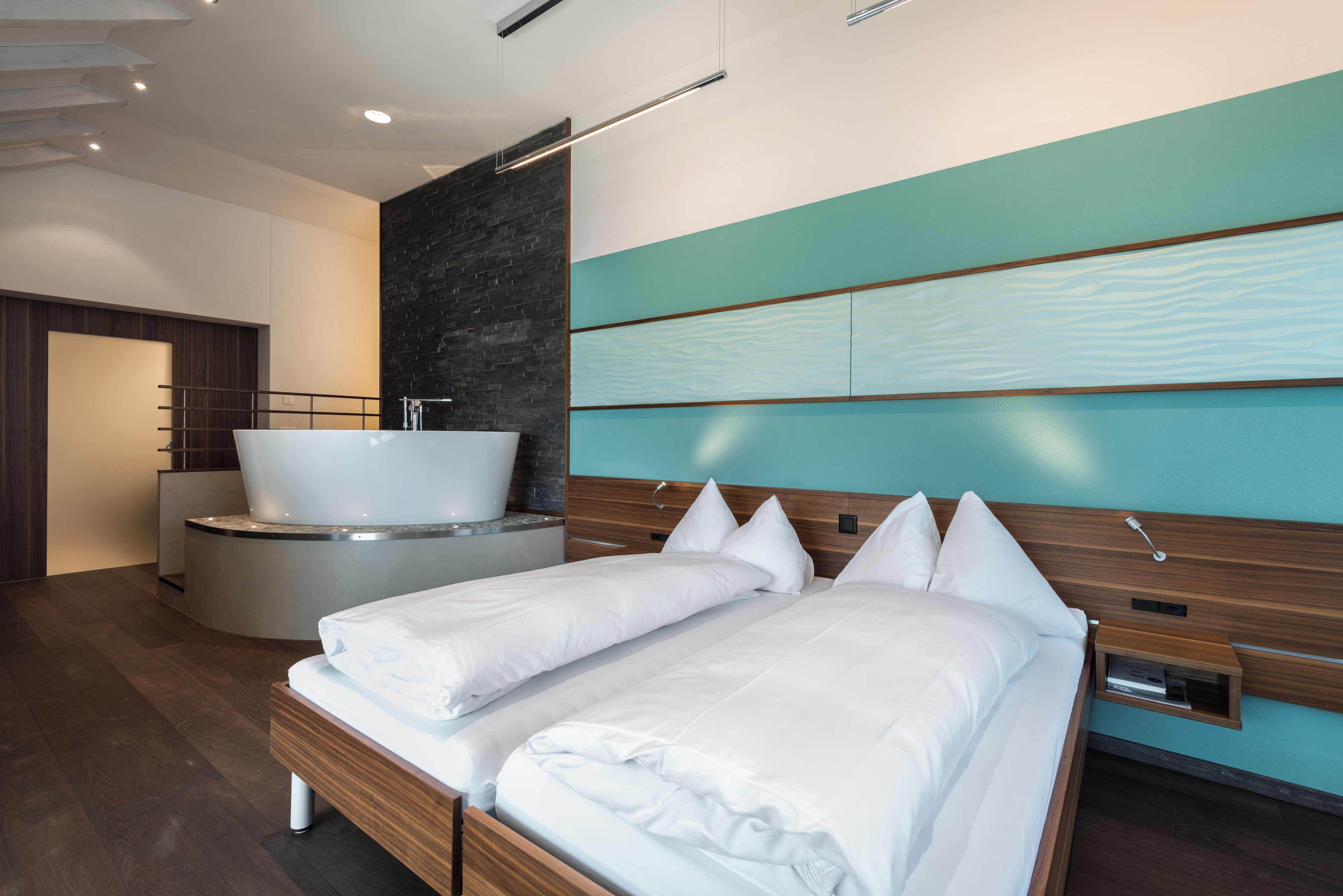 Una camera d'albergo moderna con un letto grande, una vasca da bagno tonda e una testiera in legno.