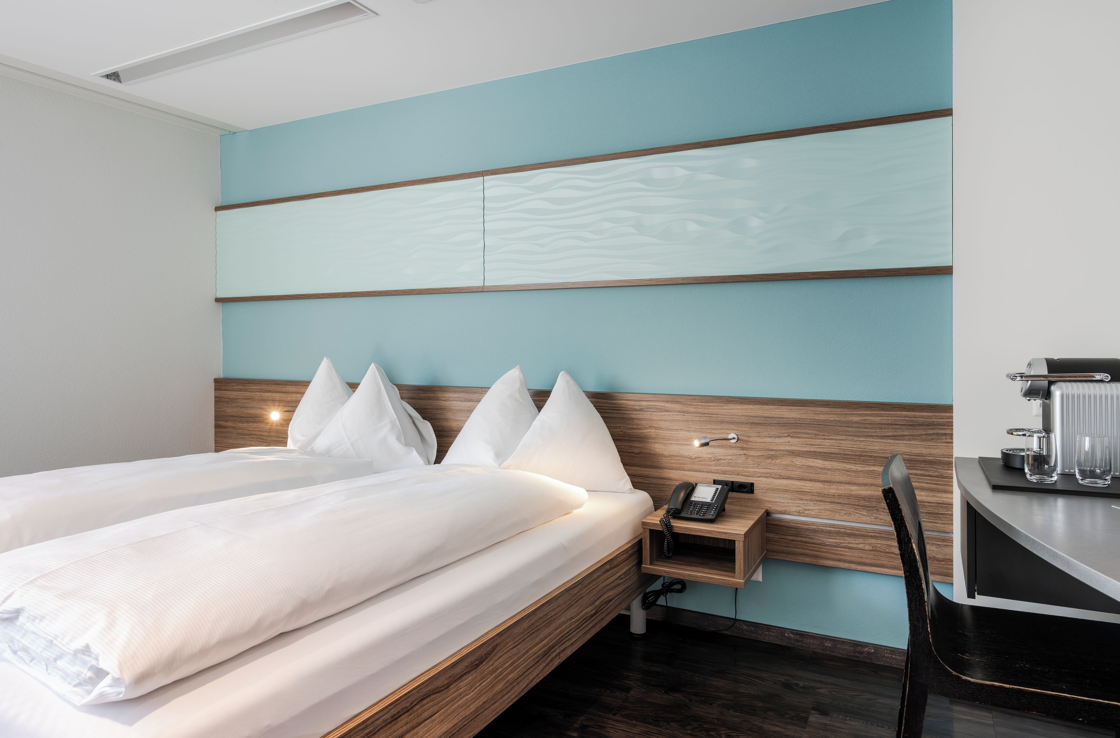 Ein Hotelzimmer mit einem Bett, einem Nachttisch und einem Schreibtisch mit Telefon und Brille.