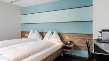 Ein Hotelzimmer mit einem Bett, einem Nachttisch und einem Schreibtisch mit Telefon und Brille.