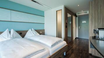 Ein Hotelzimmer mit zwei Betten, einem Holz-Kopfteil, einer blauen Akzentwand, Holzboden und einer Küchenzeile.