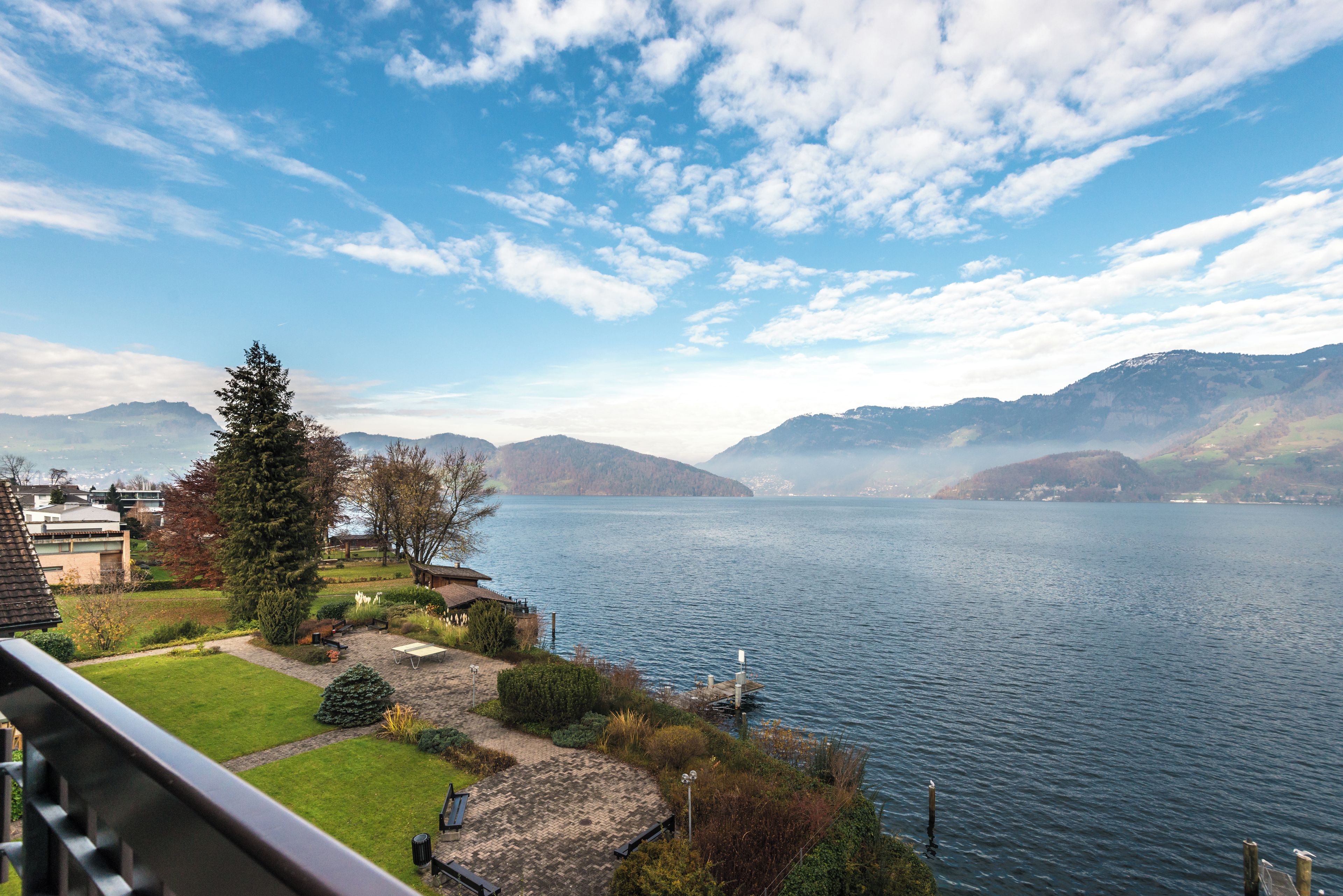 Een landgoed aan het meer met uitzicht op bergen, een houten steiger en een keurig onderhouden tuin.