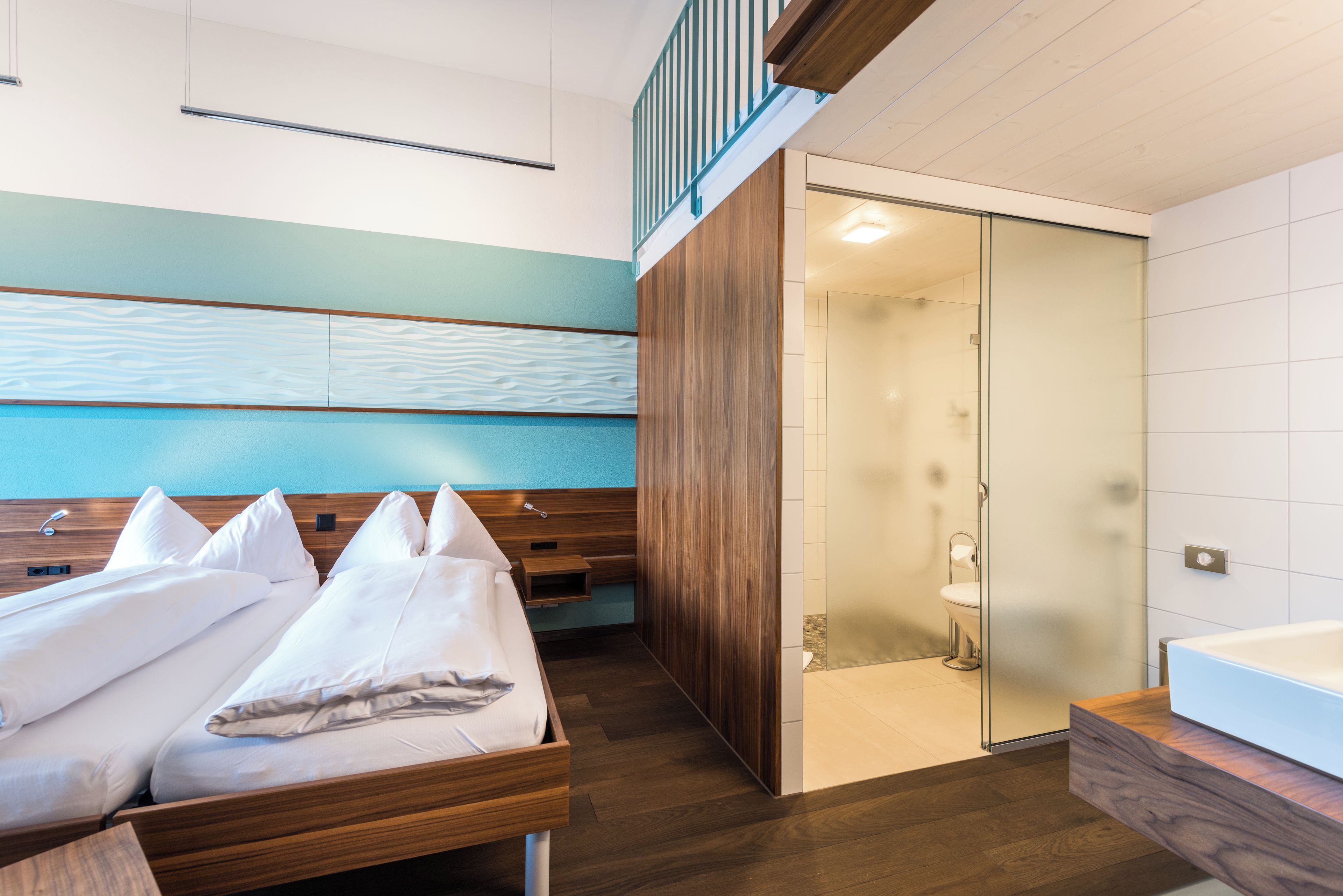 A modern hotel room with a wooden bed, a walk-in closet, and a glass-enclosed shower area.