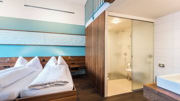 A modern hotel room with a wooden bed, a walk-in closet, and a glass-enclosed shower area.