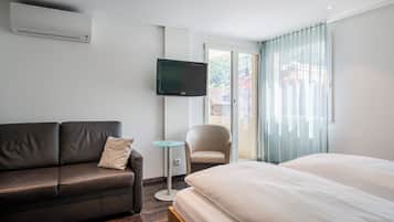 Una camera d'albergo con un letto, un divano, un tavolino, una sedia e un televisore montato a parete.
