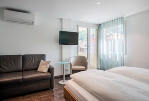 Una habitación de hotel con una cama, un sofá, una mesita, una silla y un televisor instalado en la pared.