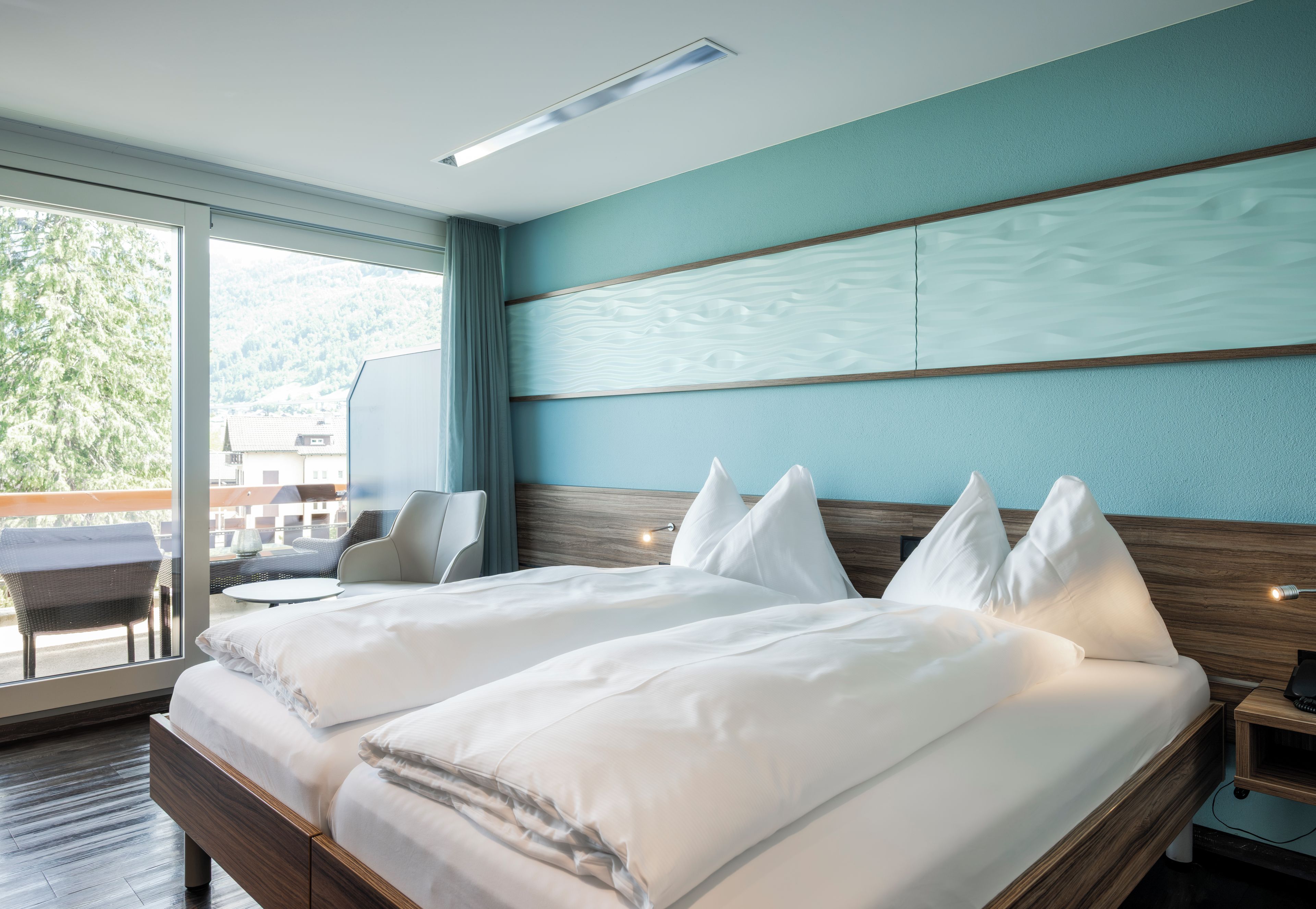 A hotel room with a large bed, a chair, a table, and a view of the outdoors.