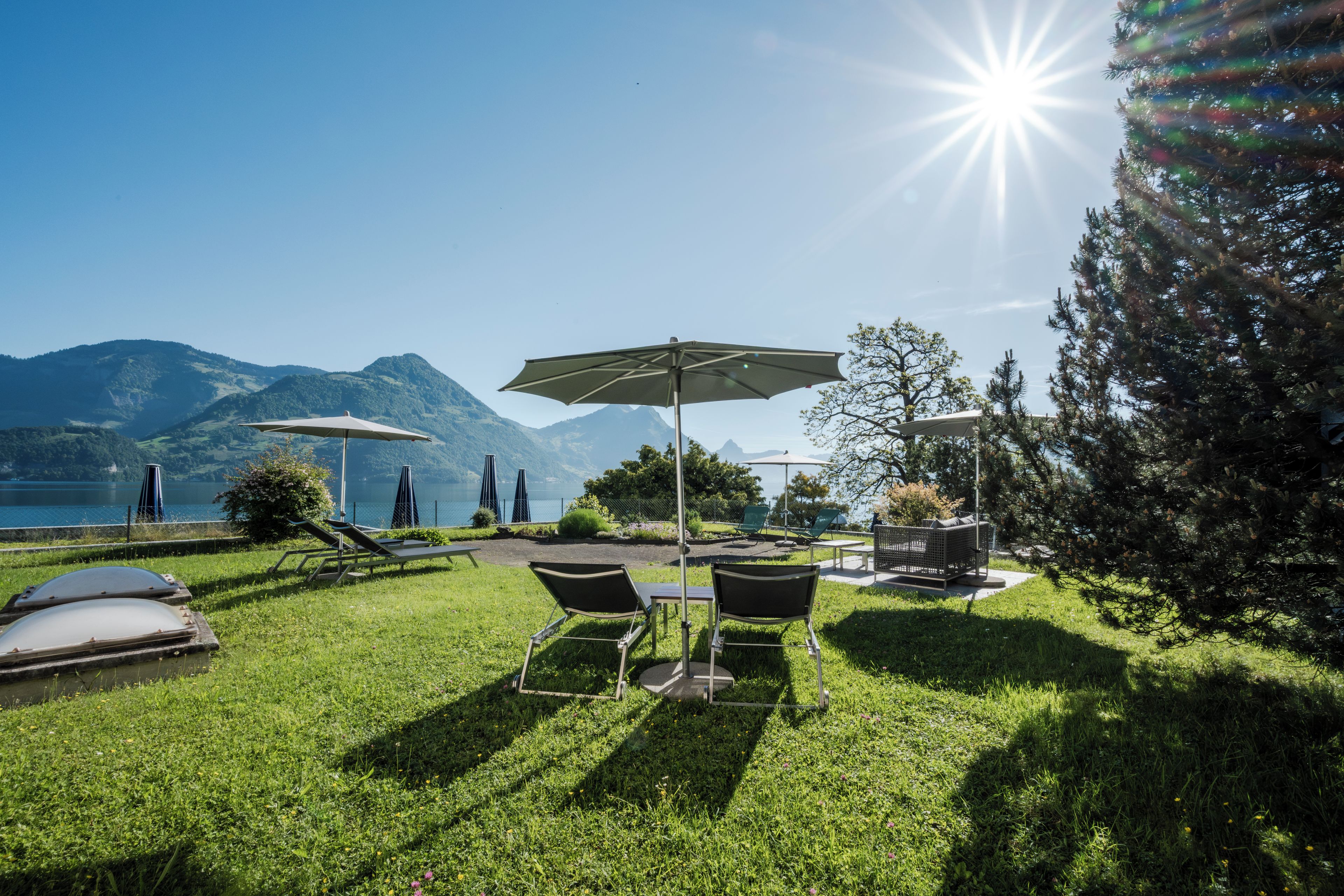 Un'area verde all'aperto con tavolo e sedie, un ombrellone e vista su montagne e lago.