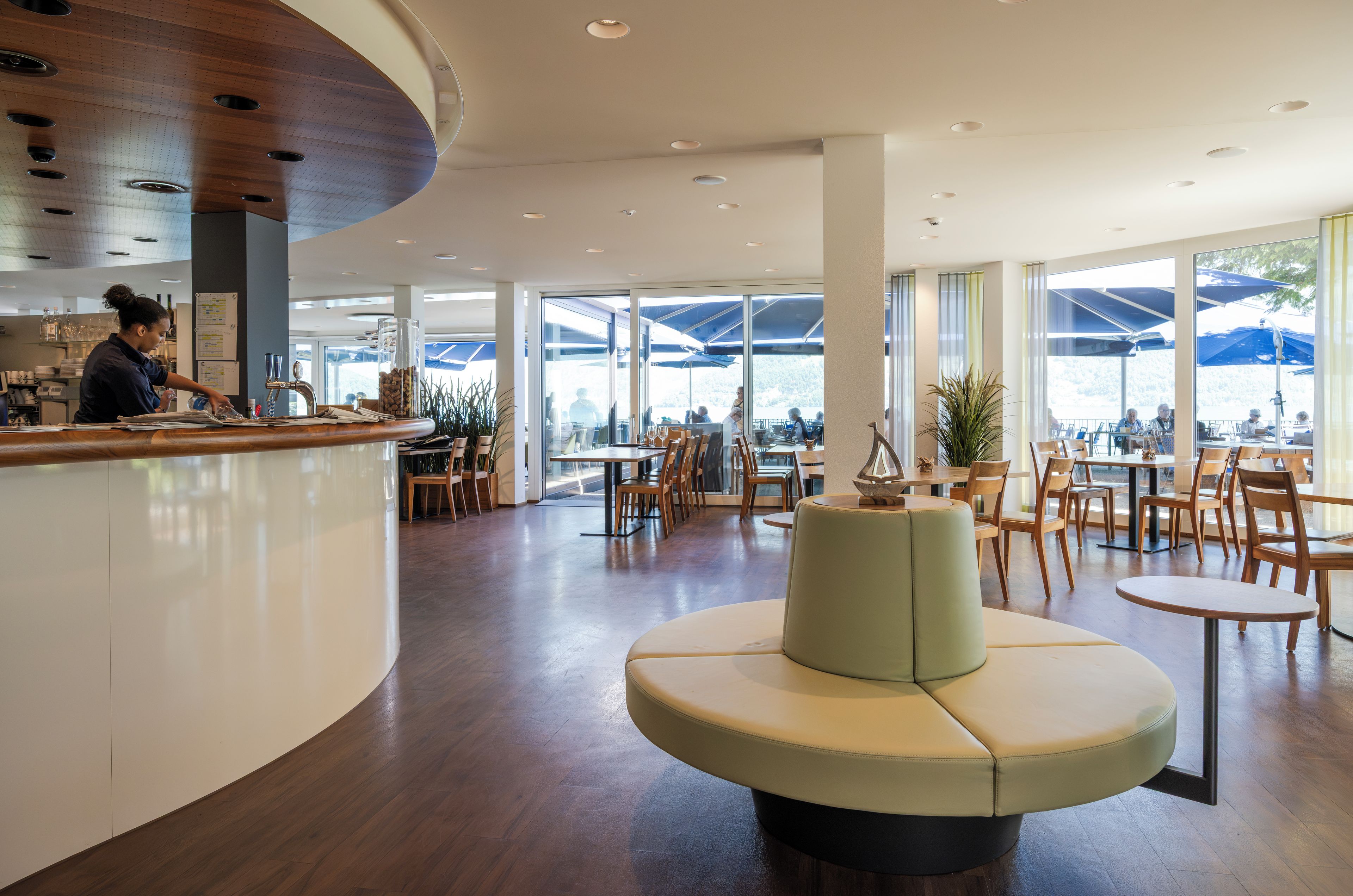 A modern interior with a curved counter, seating area, and large windows.