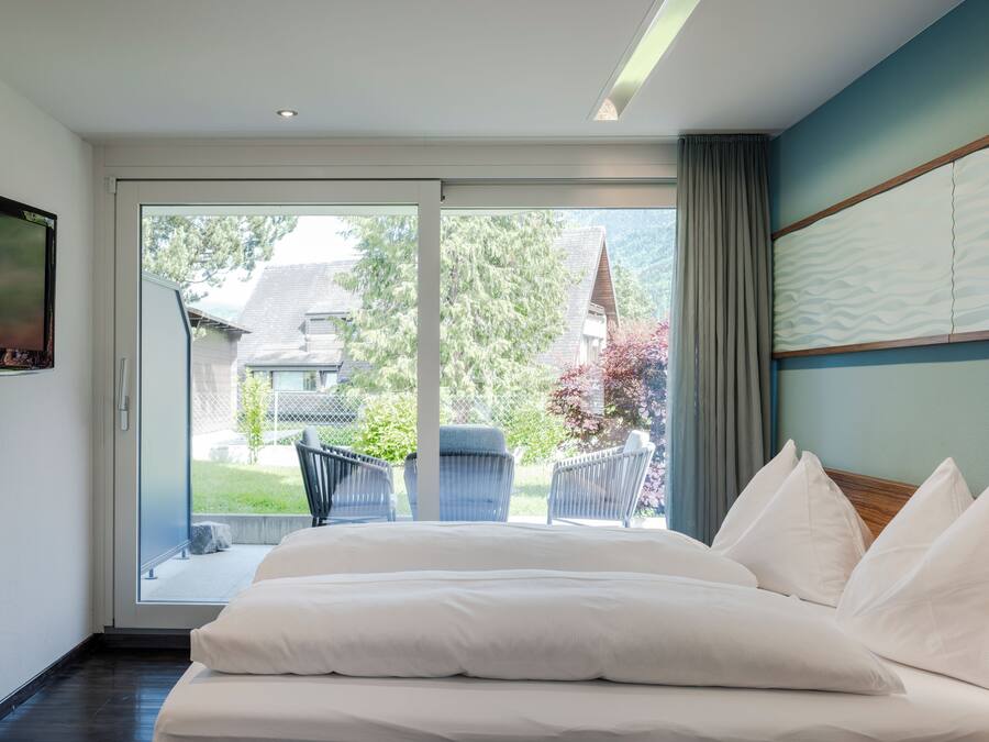 Un dormitorio con una cama grande, un televisor en la pared y un ventanal corredizo que da a un balcón.