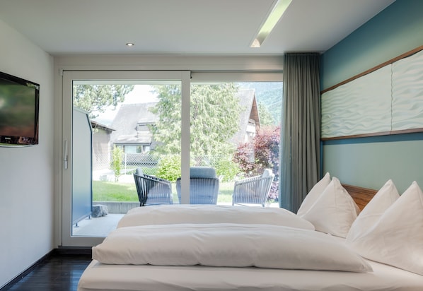 Un dormitorio con una cama grande, un televisor en la pared y un ventanal corredizo que da a un balcón.
