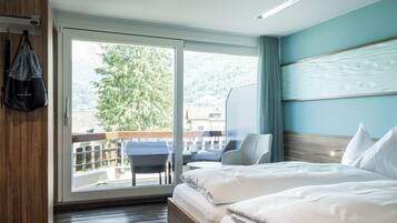 Ein Hotelzimmer mit Bett, Stuhl, Schreibtisch und Blick auf einen Balkon sowie Bäume.
