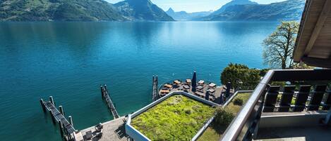 Terraza junto al lago con mobiliario exterior y vistas a una cordillera.