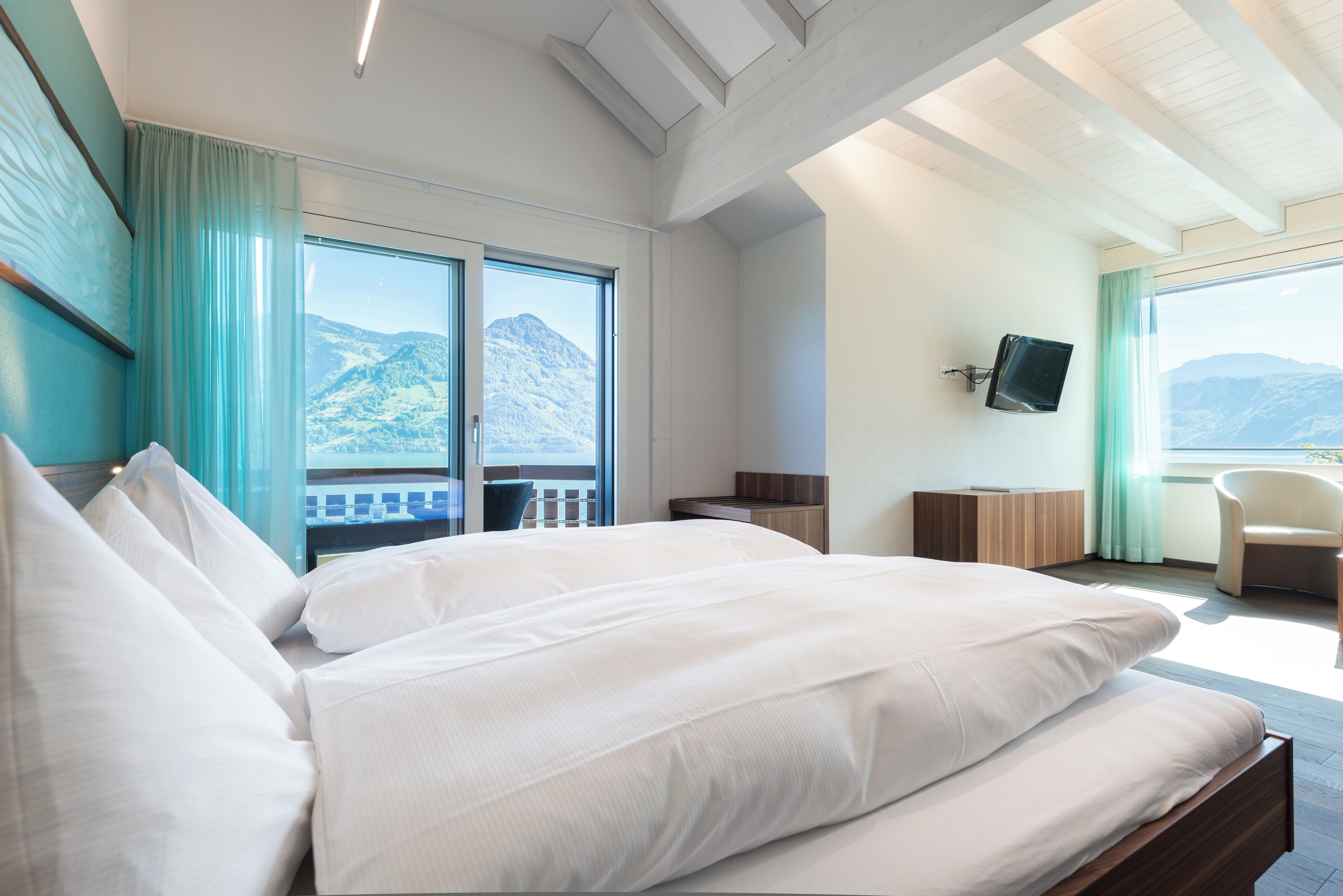 A hotel room with a large bed, a TV mounted on the wall, and a view of mountains through the window.