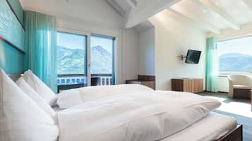 A hotel room with a large bed, a TV mounted on the wall, and a view of mountains through the window.