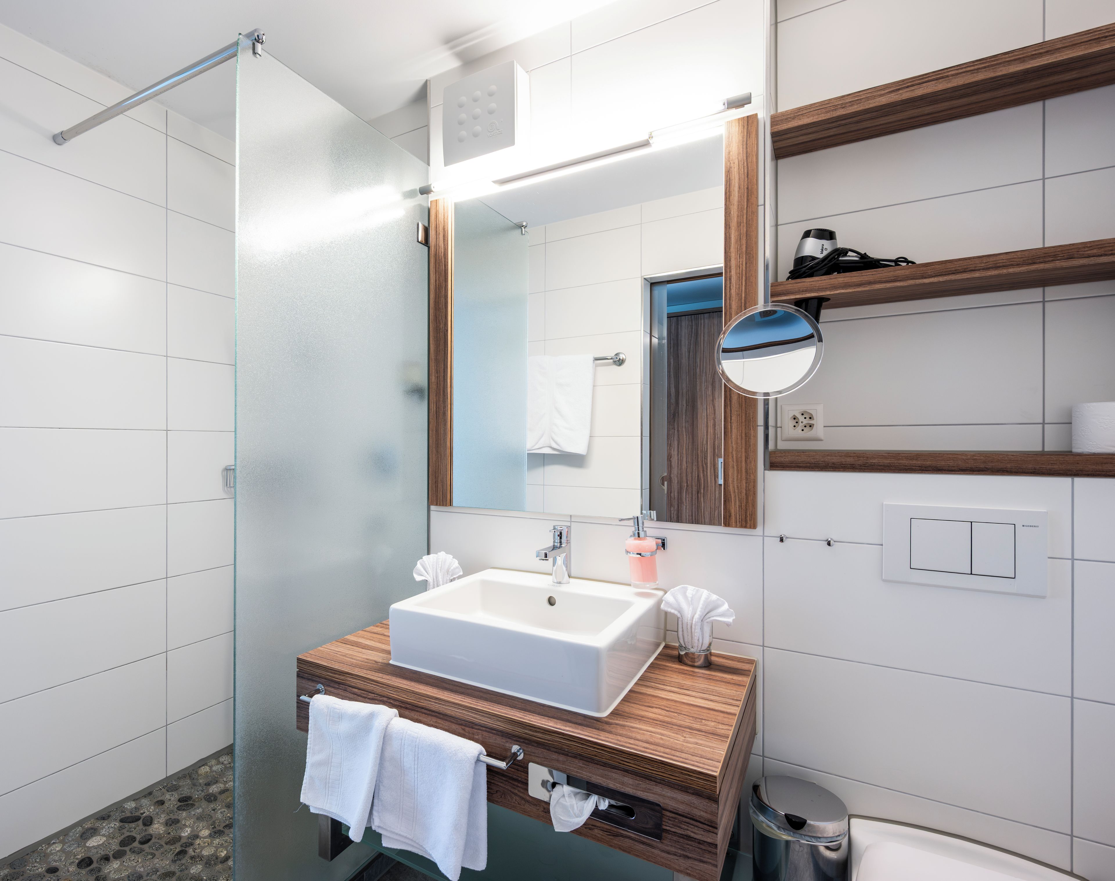 Un baño moderno con cabina de ducha de vidrio, lavamanos blanco y tocador de madera.