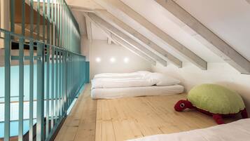A room with a sloped ceiling, wooden flooring, a bed with white bedding, a green turtle plush toy, and a blue railing.