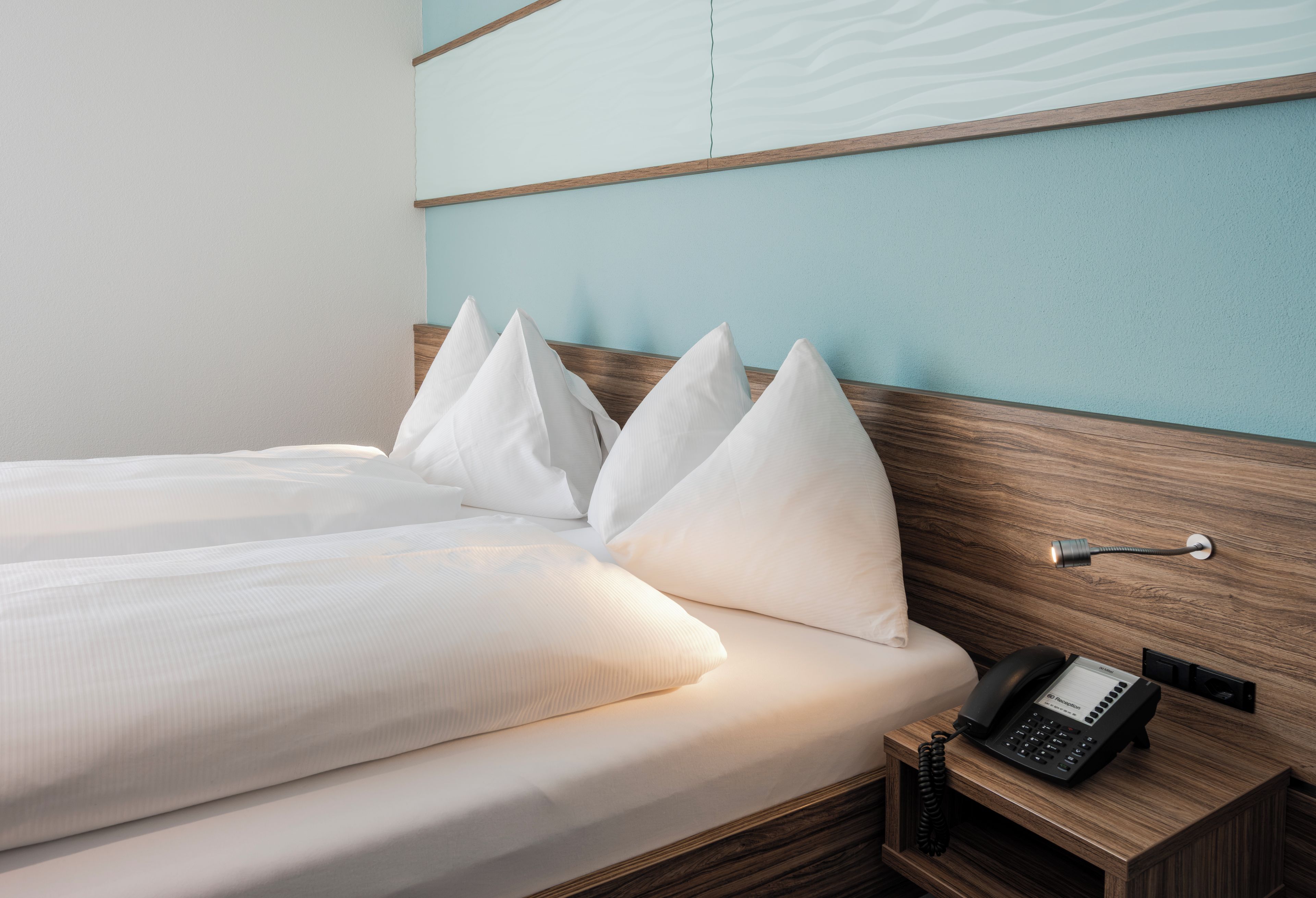 Ein Hotelzimmer mit einem Bett, Kissen, einem Nachttisch mit Telefon und einer Wandleuchte.