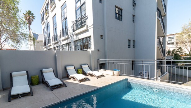 Uma piscina com espreguiçadeiras e um edifício branco com varandas.