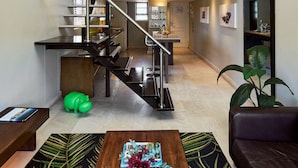 Um loft moderno com escada que dá acesso a um quarto no mezanino, área de jantar e sala de estar com uma grande janela.