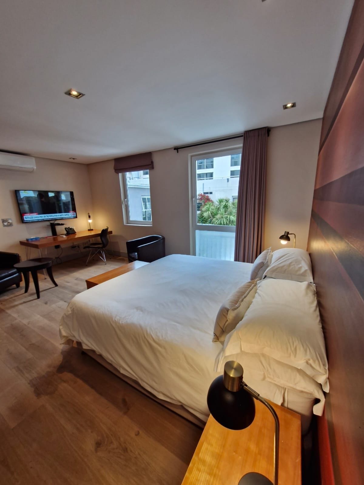 Habitación de hotel con una cama grande, un escritorio, un televisor y vistas al exterior.
