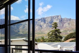 A view of a mountain range through a window, with a building and a tree in the foreground.