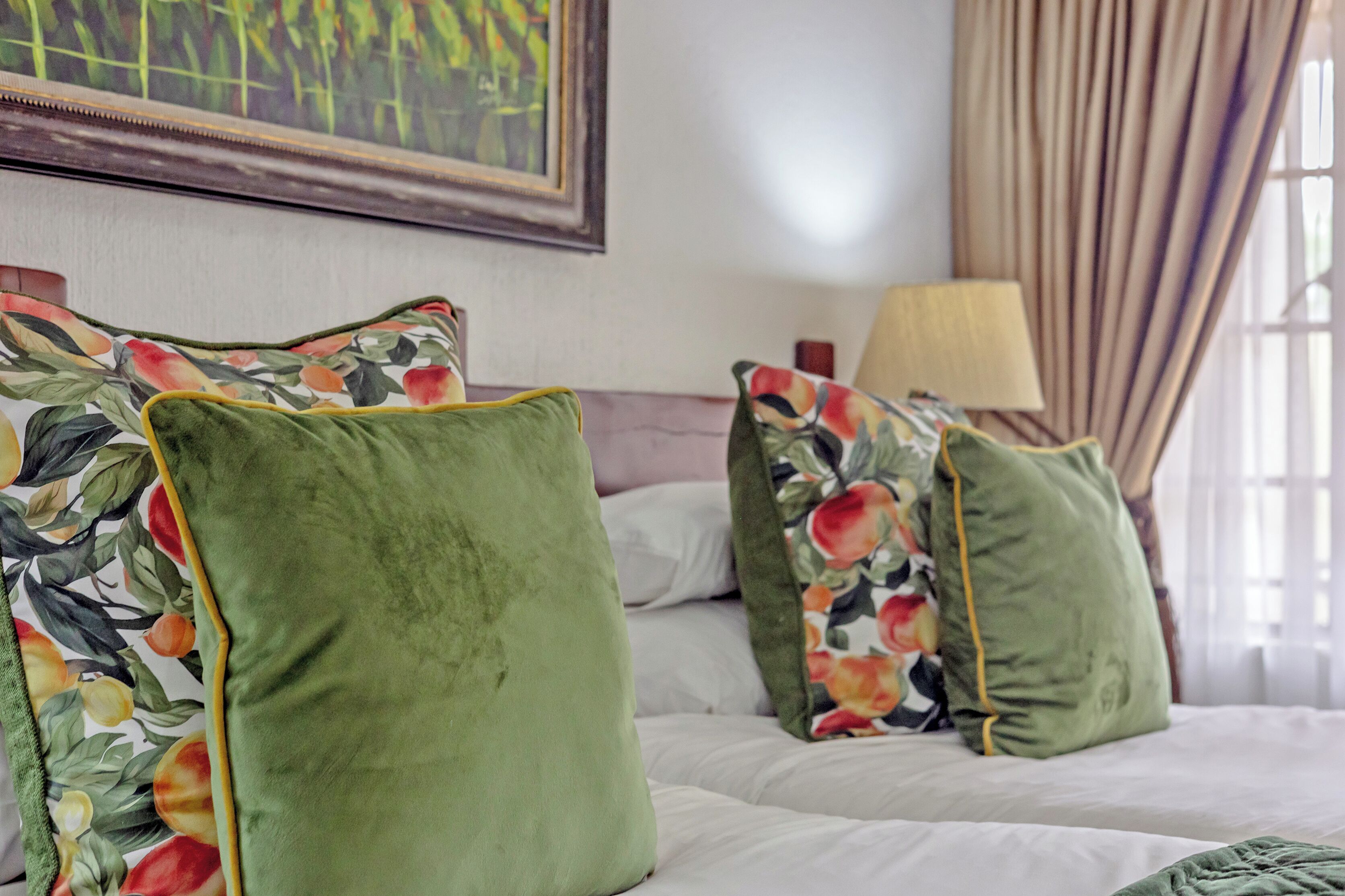 A bed with green pillows and a floral print pillowcase, a lamp, and a painting on the wall.