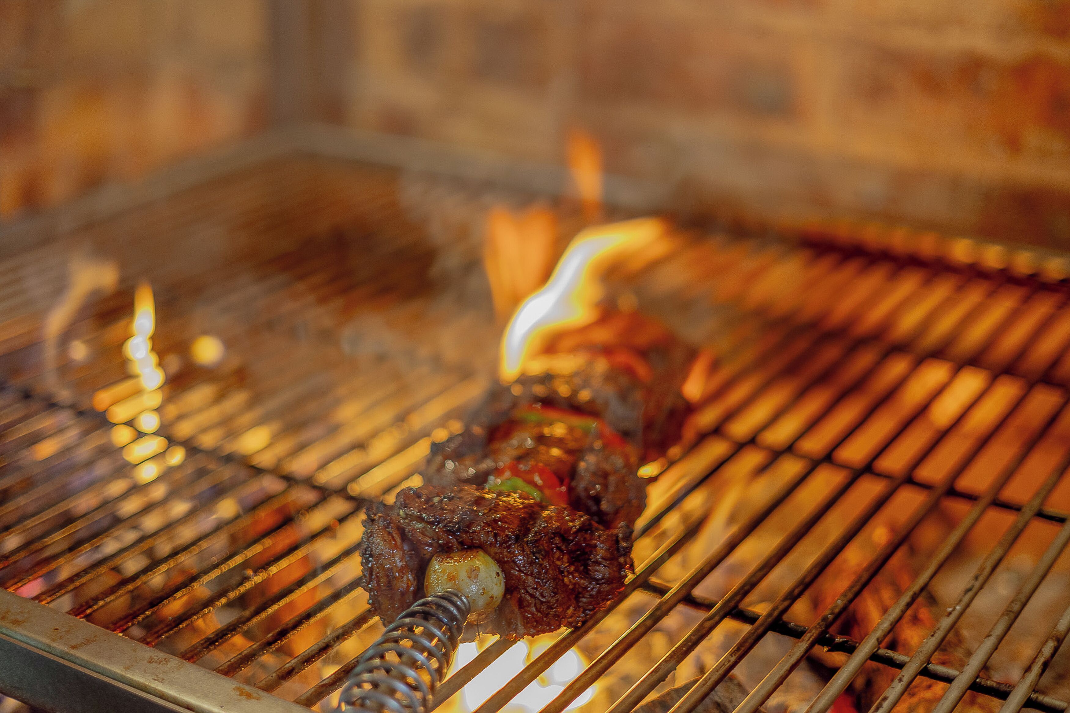 Close-up van vlees dat boven een barbecue grilt, met zichtbare vlammen en roostertegels.