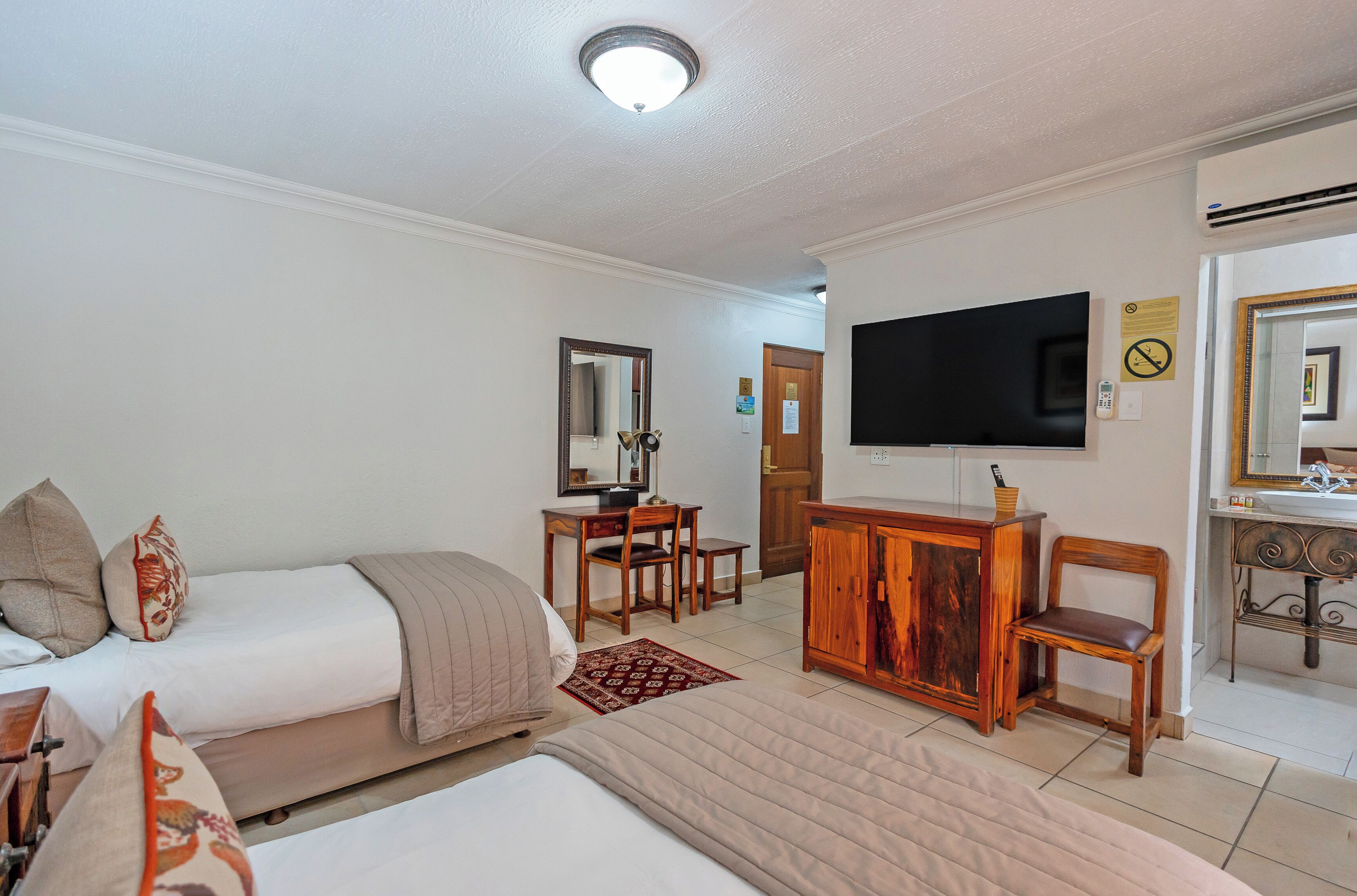 A hotel room with two beds, a desk, a TV, and a mirror.