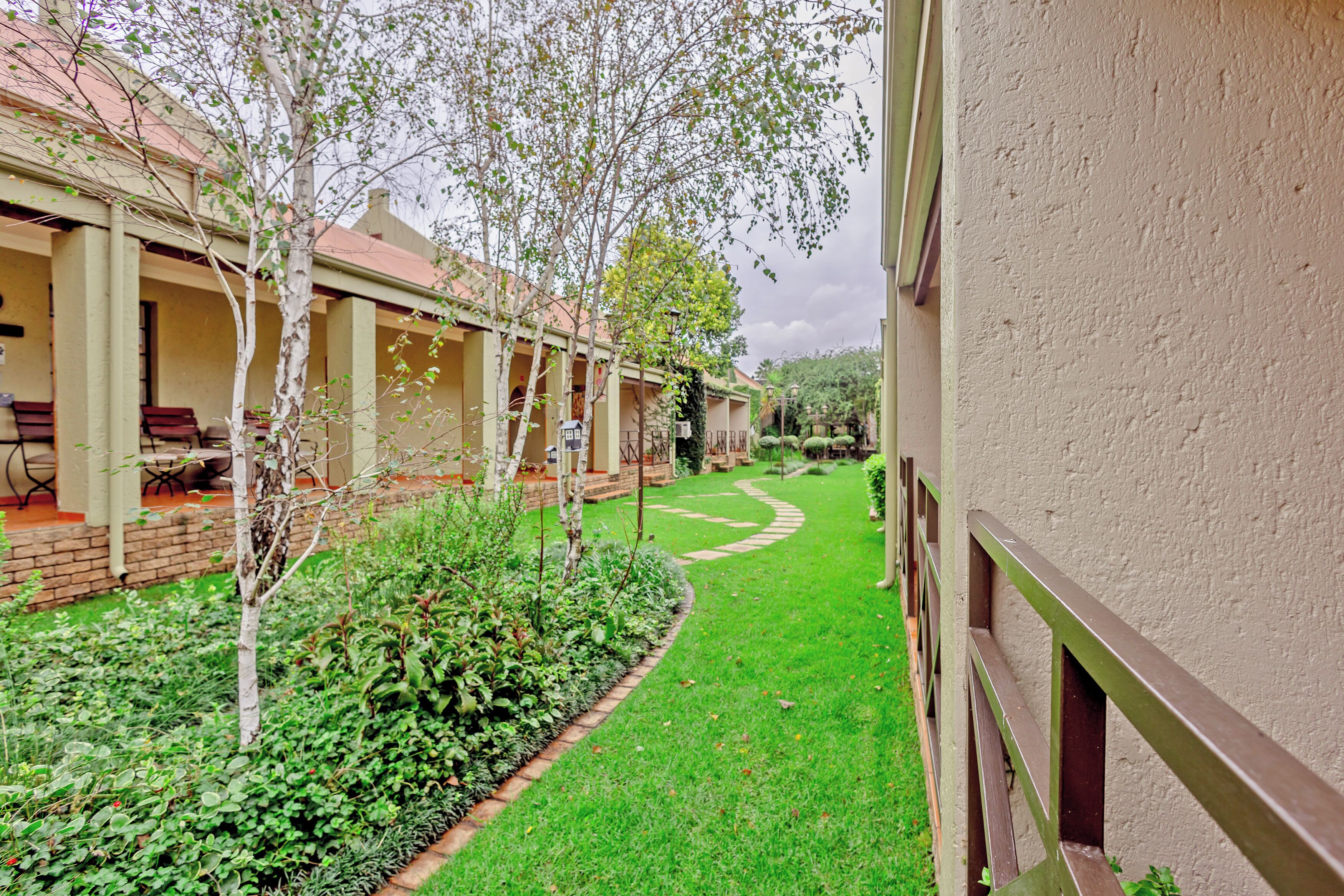 A courtyard with a pathway, a small tree, and a building with a balcony.